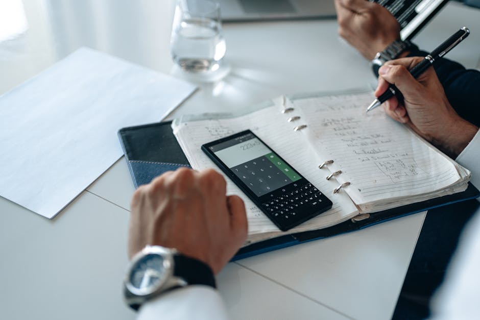 Hands using calculator and writing in notebook during business planning on a white table.