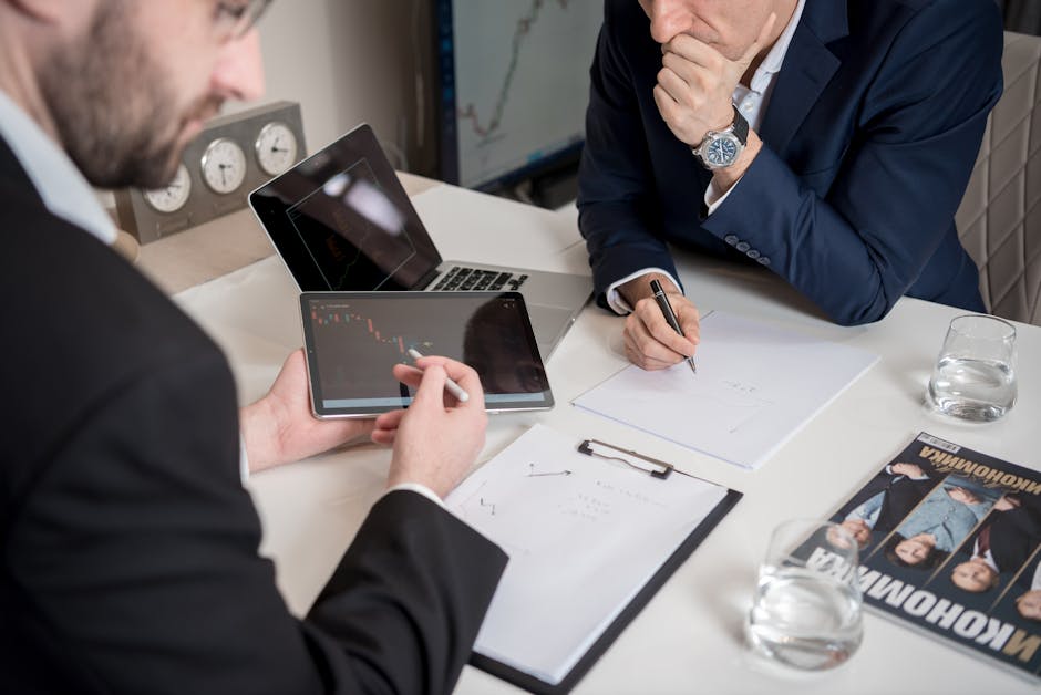 Two businessmen discussing financial charts on a tablet in a modern office setting.
